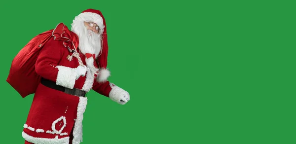 Santa claus on green with a big red bag goes and looks into the camera. Copy space. Christmas and New Year concept — Stock Photo, Image