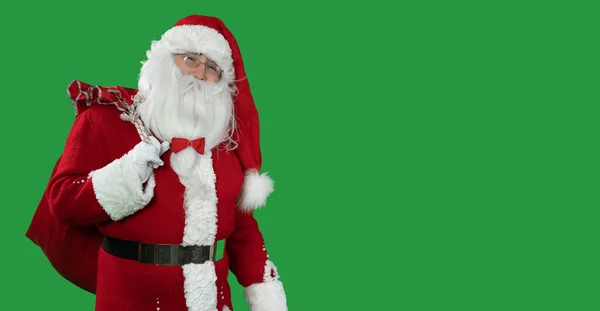 Yeşil arka planda büyük kırmızı çantalı Noel Baba kameraya bakıyor. Uzayı kopyala Noel ve Yeni Yıl kavramı — Stok fotoğraf