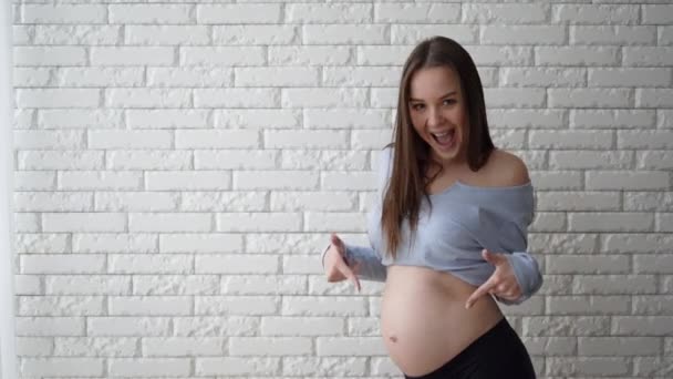 Une femme d'apparence européenne se tient près du mur, un sourire sur son visage. avec index pointant vers l'estomac. Espace de copie — Video