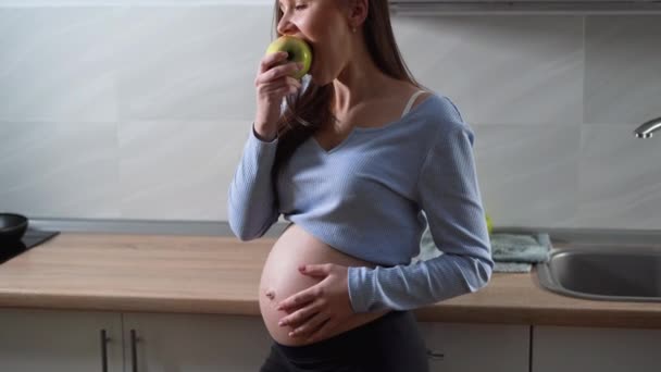 Egy európai megjelenésű terhes nő portréja áll a konyhában. Almát eszik. Fénymásolási hely — Stock videók