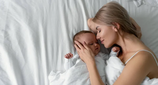 Una joven madre yace en una cama con un bebé recién nacido en la habitación. Familia feliz. Protección del niño. — Foto de Stock