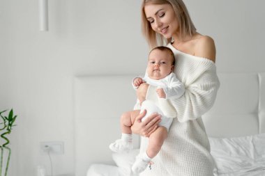 Annem yeni doğmuş bebekle yatakta oturuyor. Kadın bebeği iki eliyle tutup kafasına dokunuyor..