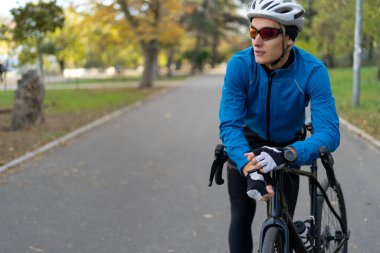Gözlüklü ve koruyucu bisiklet kasklı bir sporcu bisiklet yolundaki parkta duruyor. Spor ve açık hava eğlencesi..