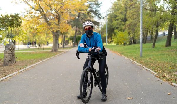 Güvenlik gözlüğü takan, siyah maske takan ve parktaki bisiklet yolunda bisiklet kaskı takan bir adam. Karantina sporları.