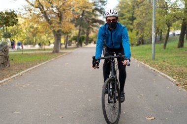 Koruyucu maskeli ve kasklı bir adam yolda bisiklet sürüyor. Karantinada dinleniyor. Fazla kiloyla savaşmak..