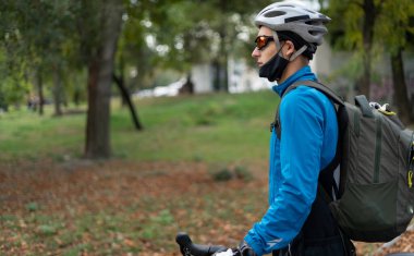 Parkta bisikleti olan Kafkas kökenli bir adam. Sporcu tatilde. Karantina ve koruyucu sağlık maskesinde yiyecek teslimatı.