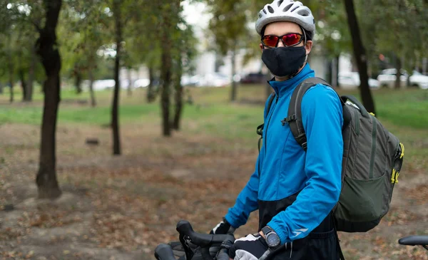 Ein Mann kaukasischer Nationalität im Park mit Fahrrad, Helm und Schutzmaske. Essenslieferung und Outdoor-Sport in Quarantäne. — Stockfoto