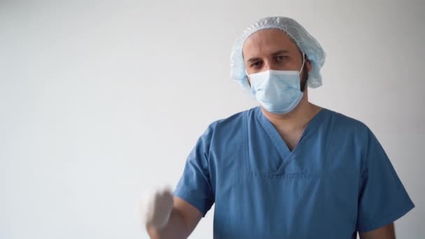 Un médecin masculin portant un masque médical sur fond blanc tient ses mains d'un poing et sort ses doigts un par un. Compter de un à cinq. — Video