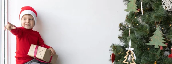 Küçük Çocuk Pencerede Oturmuş Kafasında Noel Baba Şapkası Olan Bir — Stok fotoğraf