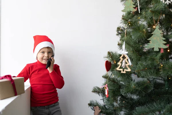 Årig Pojke Står Nära Fönstret Tomtehatt Och Pratar Telefon Julhälsningar — Stockfoto