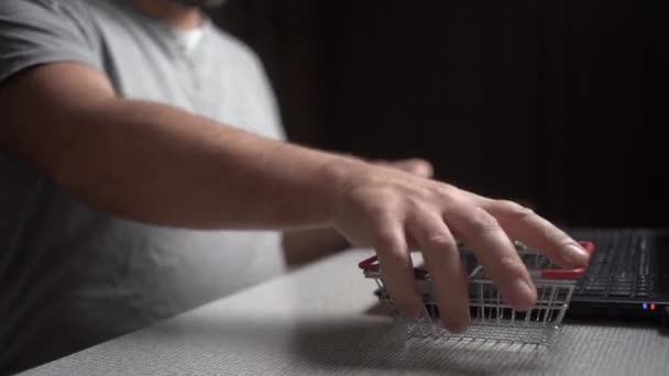 Mains mâles gros plan mettre un panier près de l'ordinateur portable et entrez des numéros sur le clavier. Achats en ligne — Video