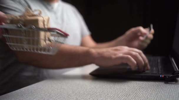 Manos están escribiendo números en el teclado y una mano femenina pone una cesta de la compra con una caja en la mesa. concepto de regalo de compras en línea — Vídeos de Stock