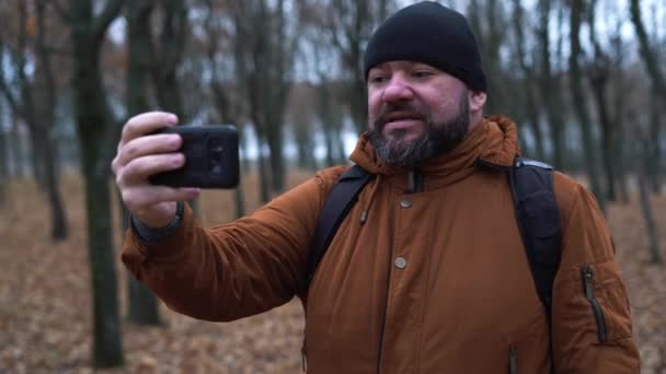 Herbstlicher Mann mit schwarzem Hut und brauner Jacke im Wald. Macht einen Videoanruf auf seinem Handy. — Stockvideo