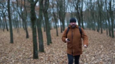 Sonbahar ormanındaki adam. Yürür ve telefonu elinde tutar, güzergaha bakmayı bırakır ve yolculuğa devam eder.