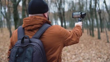 Erkek bir video blogcusu telefonda doğa görüntüsü çekiyor. Akıllı telefonlar için elektronik dengeleyici