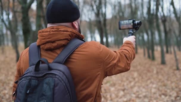 Un video blogger masculino hace imágenes de la naturaleza por teléfono. Estabilizador electrónico para smartphones — Vídeos de Stock