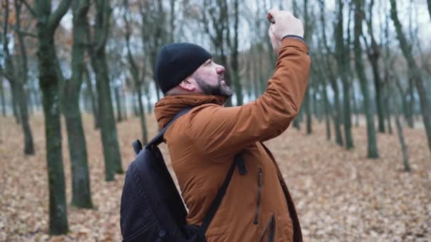 Homem com barba na floresta faz fotos da natureza no telefone. — Vídeo de Stock