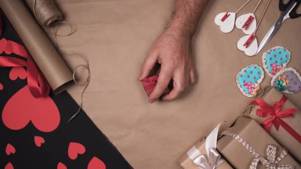 One male hand rotates a small red box on the table. Hearts and wrapping paper. Valentines day gifts concept — Αρχείο Βίντεο