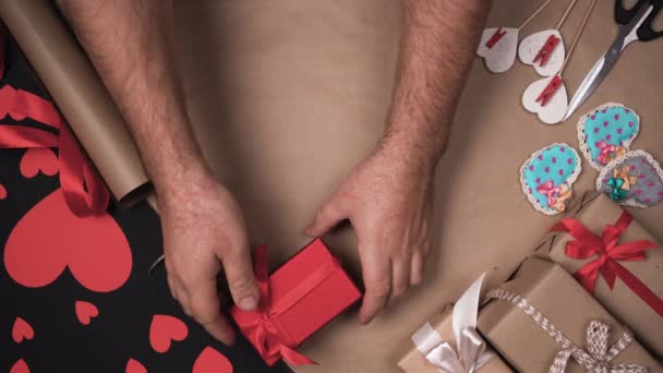 Erkek elleri masadan saten kurdeleli kırmızı bir kutu alır. Yayı çöz ve hediyeyi aç. Sevgililer Günü sürpriz konsepti. — Stok video