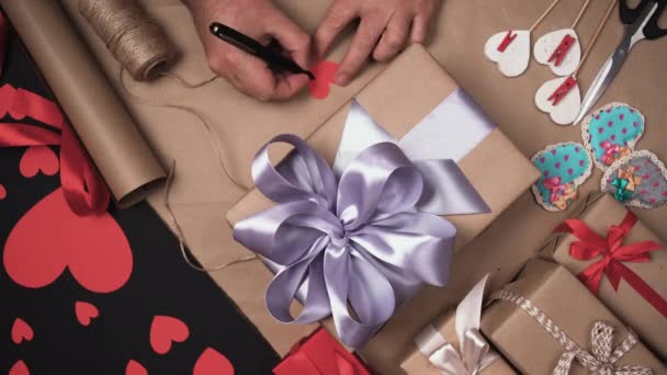 Les mains masculines écrivent la phrase que je t'aime sur une feuille en forme de cœur. Signez le cadeau. Concept surprise Saint-Valentin. — Video