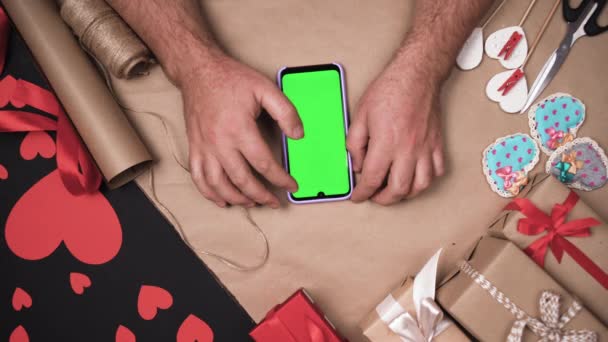 Mãos masculinas fazendo compras de presentes para dia dos namorados on-line usando um smartphone. Fundo verde, espaço de cópia. — Vídeo de Stock