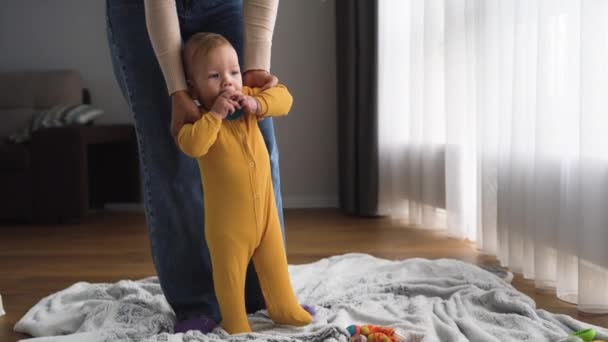 Un bambino, un ragazzo di 6 mesi, cammina con sua madre in giro per la stanza e rode un giocattolo. Concetto famiglia felice — Video Stock