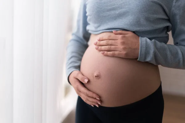 Una embarazada está cerca de la ventana. Vientre cerca. Las manos lo tocan. El concepto de comunicación con el bebé antes del parto — Foto de Stock