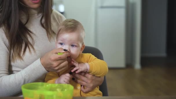 Kaukázusi kisfiú portréja. Az anyám ölében ül és zöldséges pürét eszik. Megetetni a babát egy kanállal.. — Stock videók