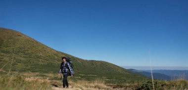 Büyük sırt çantalı bir erkek turist dağ yamacına tırmanıyor..