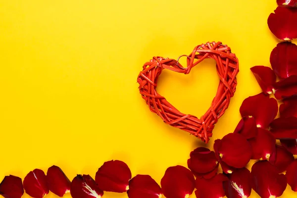 Plano laico, corazón rojo se encuentra sobre un fondo naranja cerca de pétalos de rosa. Concepto para celebrar el día de San Valentín. Copiar espacio. — Foto de Stock