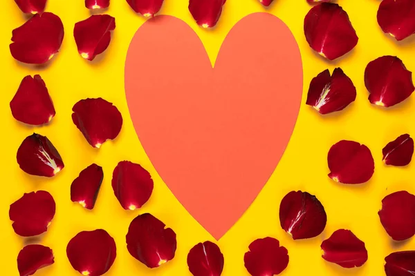 Gran corazón rojo en pétalos de rosa sobre fondo amarillo. Copiar espacio. Concepto para celebrar el día de San Valentín — Foto de Stock