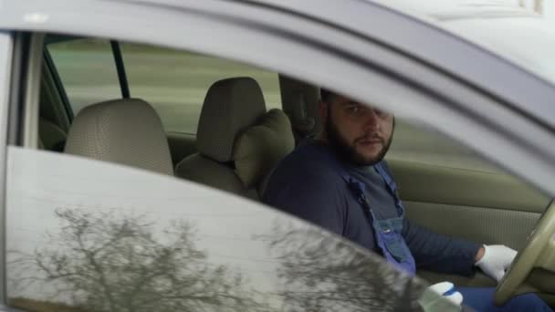 Hombre sentado en el asiento del conductor en el coche. Él baja el vaso y con un gesto de su mano le invita a sentarse. — Vídeo de stock