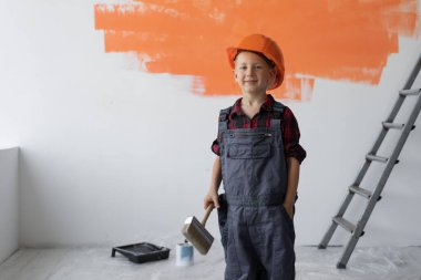 Tulum giymiş bir çocuk elinde boya fırçasıyla odada duruyor. Ev yenileme konsepti.