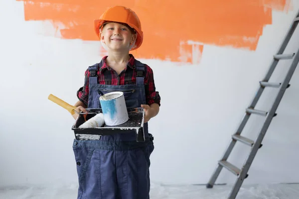 A boy dressed in overalls stands in the room holding a jar of paint in his hands, a smile on his face. Home renovation concept. — Stock Photo, Image