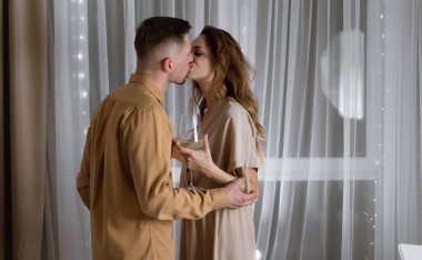 Genç bir çift ellerinde bardaklarla masanın yanında öpüşüyor. Yıldönümü konsepti, Sevgililer Günü. Boşluğu kopyala.