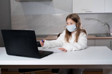Uzaktan öğrenim online eğitim. Tıp maskeli kız evde dizüstü bilgisayar ödevi yapıyor. Karantina