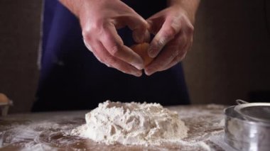 Yakından bir aşçının elleri un yığınına yumurta çakar. Konsept: tatlı, pasta, hamur, lezzet, saf ürün, pişirme, restoranlarda çalışma, pişirme