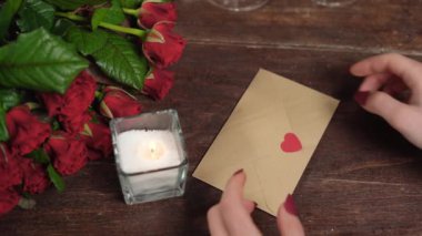 Kadınların elleri içinde kalpler olan bir mektubu açar. Masada güller ve bir mum var. Sevgililer Günü konsepti.
