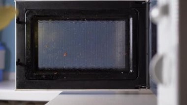 Mutfakta bez parçasıyla mikrodalga fırın temizleyen lastik sarı eldivenli ve köpüklü bir kadın..