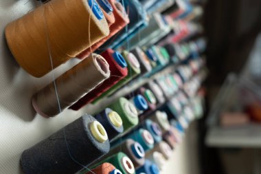 Metal bir duvara farklı renklerde dikiş iplikleri monte edilir ve dikiş atölyesinde yan görünüme yerleştirilir. Üretim ve malzeme çeşitliliği kavramı. Boşluğu kopyala.