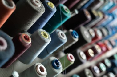 Metal bir duvara farklı renklerde dikiş iplikleri yerleştiriliyor ve dikiş atölyesindeler. Üretim ve malzeme çeşitliliği kavramı. Boşluğu kopyala.