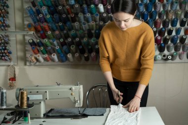 Bir terzi çalışma masasında durur ve beyaz kumaşı makasla keser. Atölyedeki terzi sevdiği şeyi yapıyor..