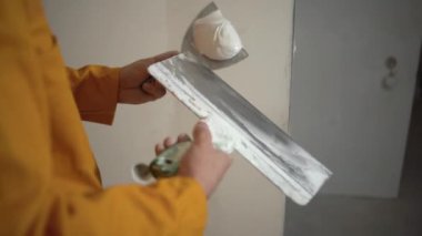 İki spatula tutan ve macunu onların yardımıyla karıştıran bir inşaat işçisinin yakın çekimi. Ev yenileme konsepti