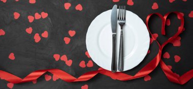 Plakalı, bıçaklı, çatallı, kırmızı kurdeleli ve siyah arkaplanlı sevgililer günü sofrası. 8 Mart ve sevgili karına bir hediye..