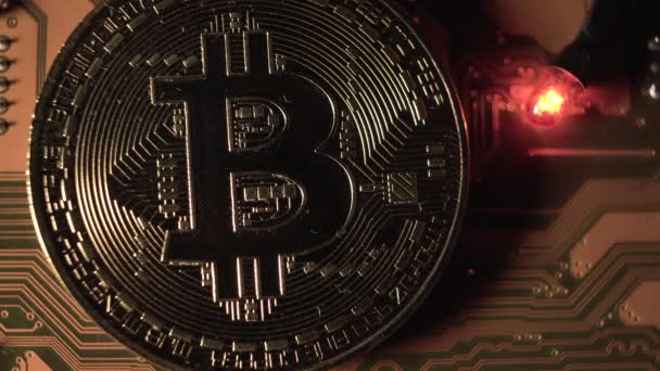 Jedna zlatá mince se symbolem bitcoinu na elektronických obvodech na základní desce počítače. Nedaleko bliká diodová lampa. Koncept těžby kryptoměn — Stock video