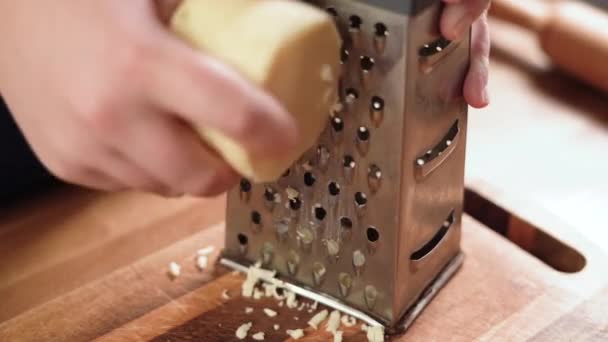 Närbild kvinnlig Hand gnider hård ost på en metall rivjärn. Osten smulas sönder smidigt på en skärbräda. — Stockvideo