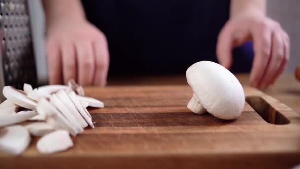 As mãos femininas pegam uma faca e cortam o cogumelo champignon em duas metades. mulher preparando jantar em casa — Vídeo de Stock