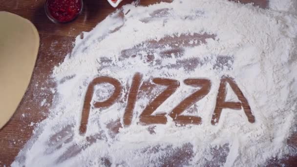 The word pizza is written with a finger on the flour, the light is flickering. — Stock Video