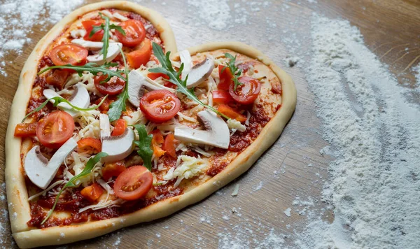 Personalized order of heart-shaped pizza for a holiday to celebrate at home. Place on the floured table in the left corner. The pizzeria is open on the eve of Valentine\'s Day.