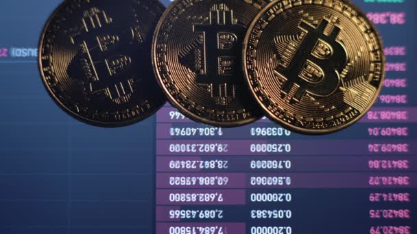 Échange en ligne, taux de crypto-monnaie. Trois pièces Bitcoin sont sur le moniteur où le prix de la monnaie est affiché en temps réel — Video